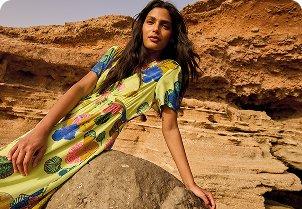 a woman in a dress sitting on a rock in the desert